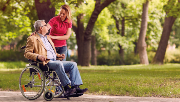 Ein Rollstuhlfahrer in einem Park im Gespräch mit einer Begleiterin