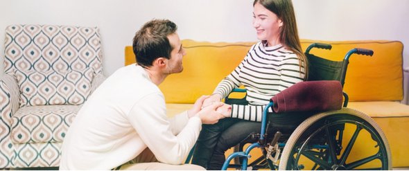 Ein Mann hält seine Partnerin im Rollstuhl an beiden Händen